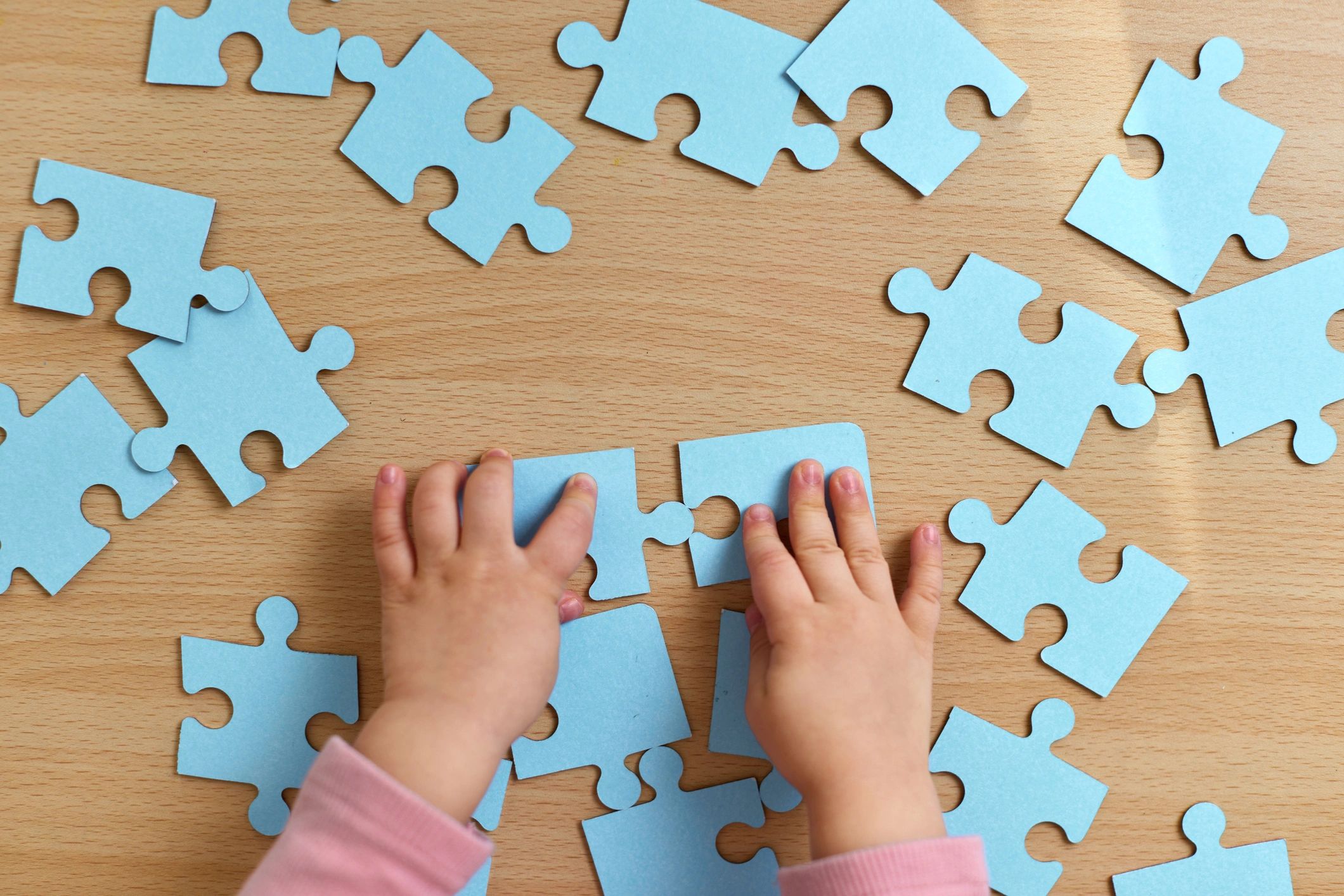 Child hands arranging blue puzzle pieces on a table