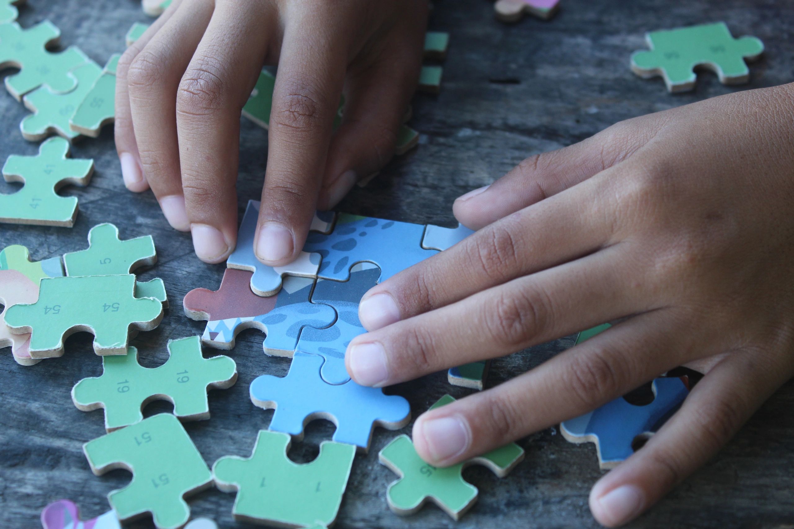 Hands assembling a jigsaw puzzle on a wooden table